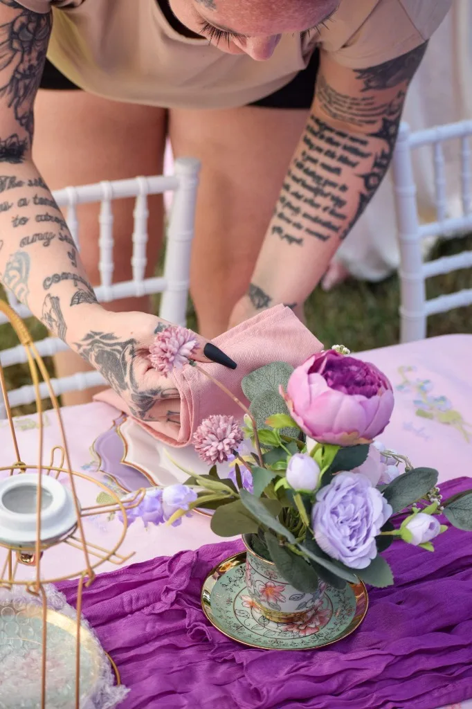 Hands draping a blush napkin along the children's tea party table during setup