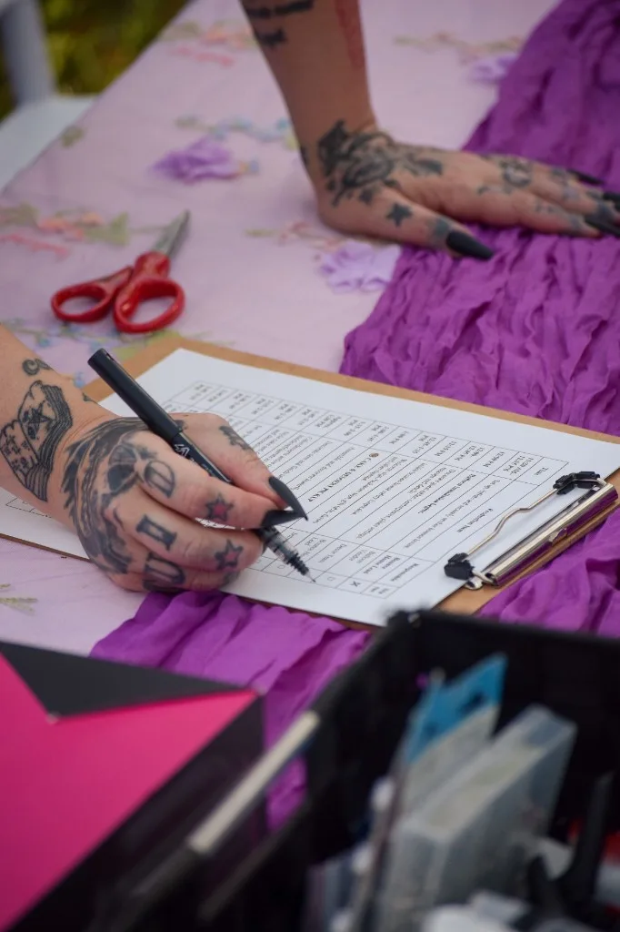 Hands checking a production plan clipboard beside purple linens during event setup