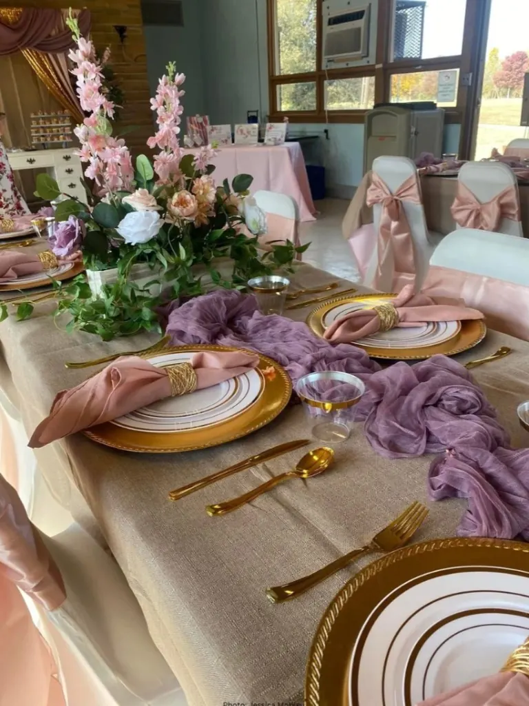 Close-up place setting with gold flatware, dusty rose napkin, and floral centerpiece