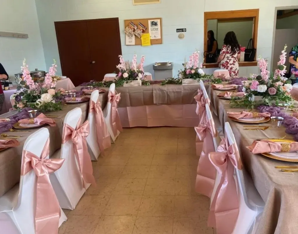 U-shaped table layout with pink linens, gold chargers, and soft floral crates