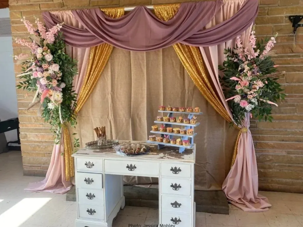 Dessert station with cupcakes and floral pillars against a draped boho backdrop
