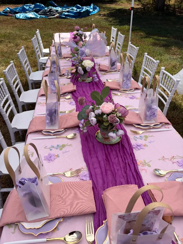 Children's dining table with embroidered pink linens, purple runner, and favor bags