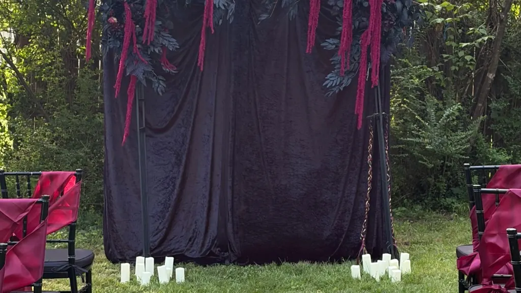 Outdoor ceremony backdrop with dark velvet draping, cascading florals, and candle clusters
