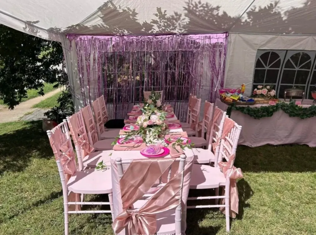 Pink party under a white tent with blush chairs, floral runner, and magenta backdrop