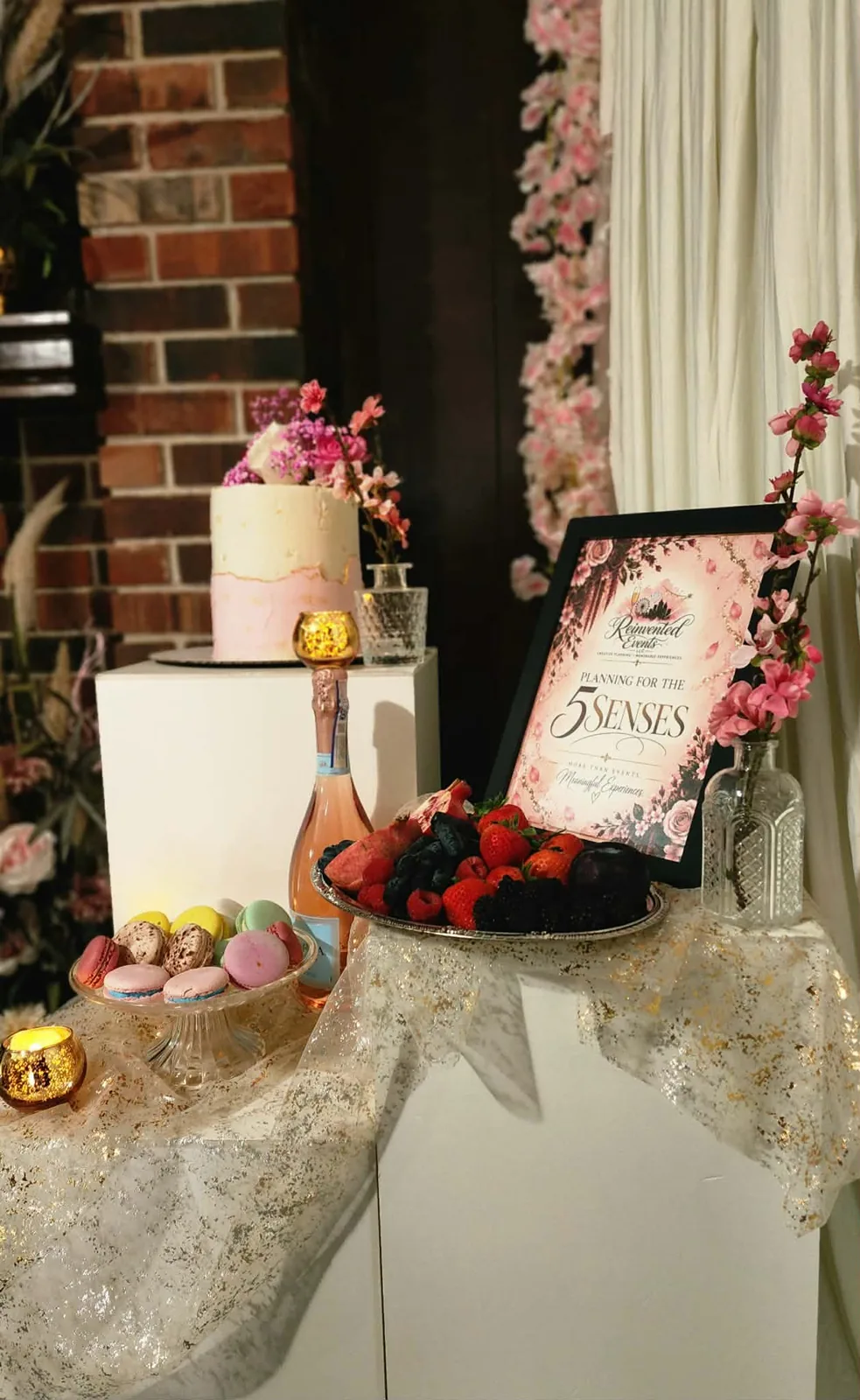 Dessert display with blush cake, macarons, berries, rosé, and a Planning for the 5 Senses sign