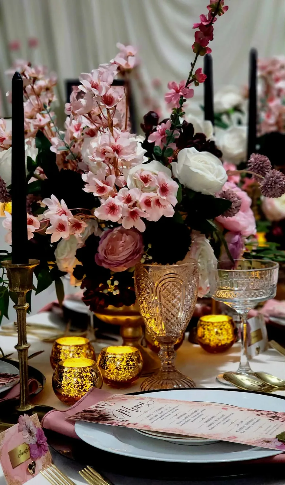 Close-up of cherry blossoms, roses, and berry-toned blooms with gold candlelight