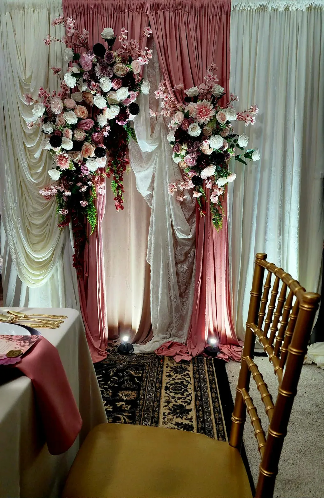 Floral backdrop beside a gold Chiavari chair and blush napkin place setting